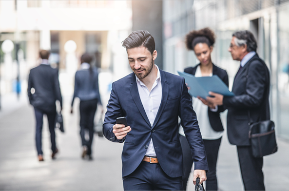 Homme en costume qui tient un téléphone et regarde ses mails en marchant